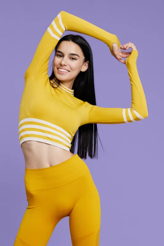 woman sport fitness in bright yellow activewear stretching arms over purple background smiling, energy and health concept, youthful athletic style, vibrant outfit