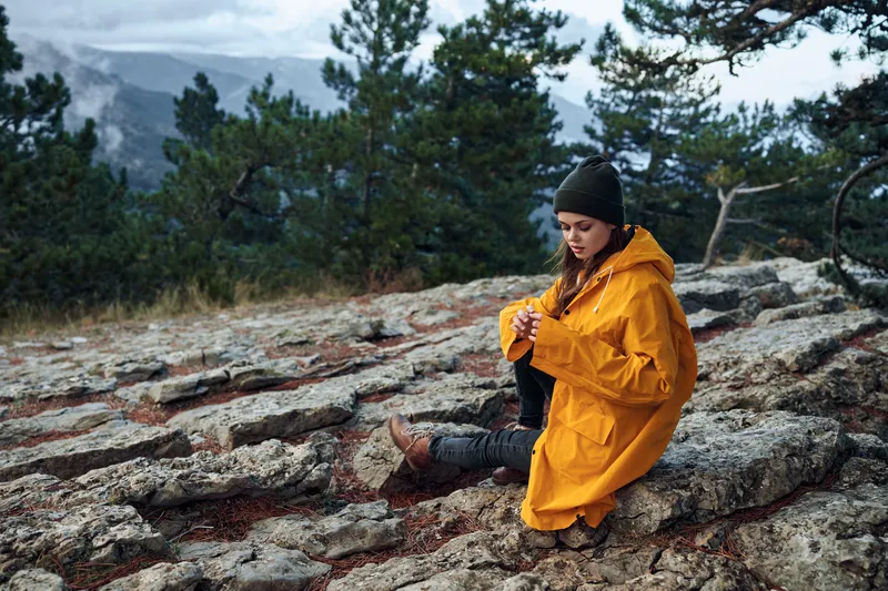Женщина-путешественница в стильном жёлтом пальто наслаждается захватывающим дух горным видом в окружении густого леса