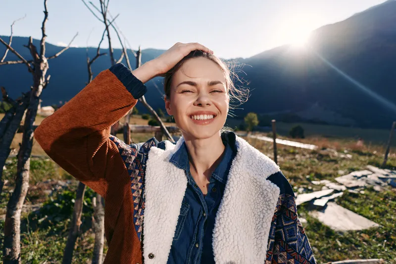 woman smile outdoor mountains sunlight portrait nature jacket, young female enjoying mountain landscape at golden hour with cozy casual outfit, candid happy expression and sun flare