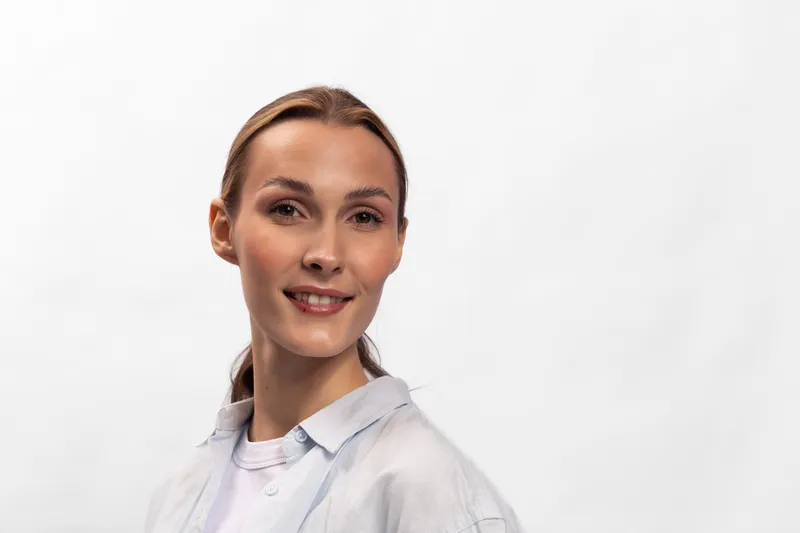 Smiling woman with light brown hair and natural makeup wears casual white shirt against white background. Concept of beauty, lifestyle, confidence, and natural portrait photography.