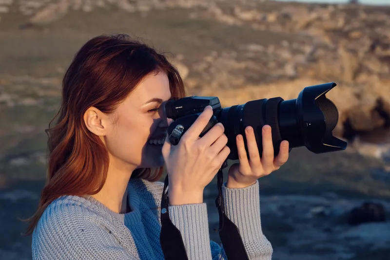Жизнерадостная женщина-фотограф профессионально работает на открытом воздухе, на фоне скалистых гор и живописного пейзажа