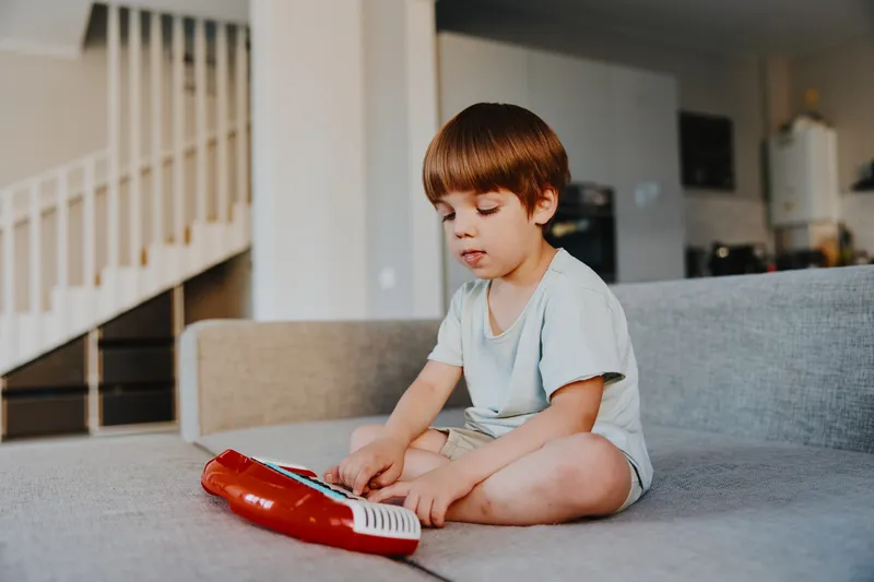 Young boy playing with a toy keyboard in a cozy living room, expressing curiosity and joy while exploring music and creativity in a home setting.
