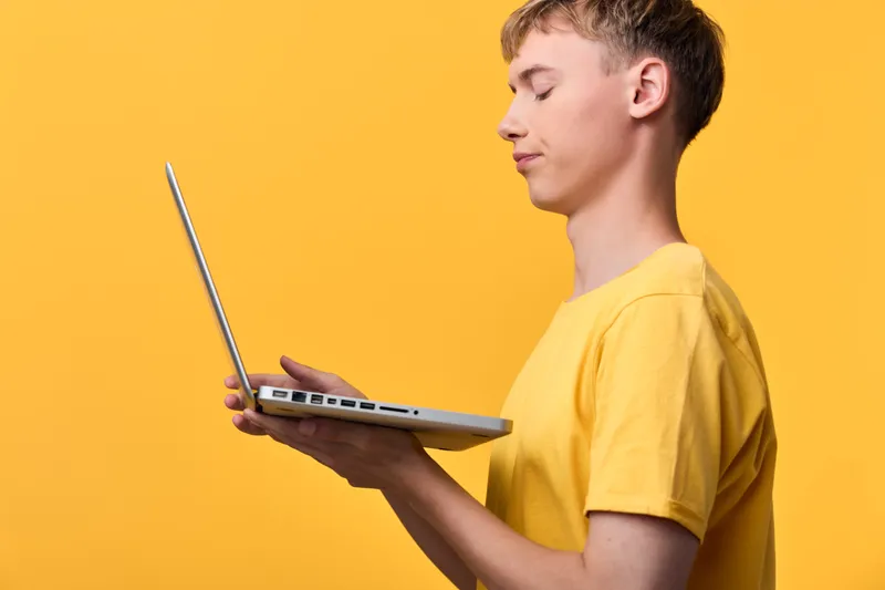 Laptop in hand, yellow backdrop, technology driven scene highlighting learning and online work with a focus on screen efficiency and digital communication