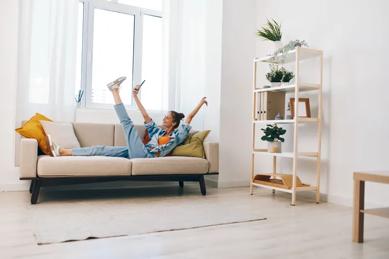 Расслабленные геймеры на диване: красивая женщина держит телефон и улыбается дома