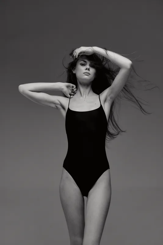 black and white portrait of a young woman in black swimsuit with flowing hair and confident expression
