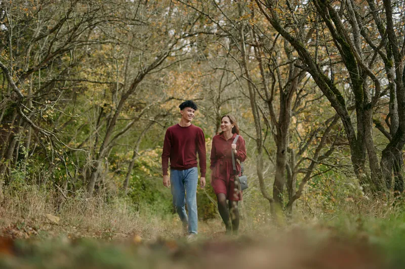A candid couple walks through a sunlit autumn forest, capturing authentic connection and genuine mood as soft light filters through trees and fallen leaves.