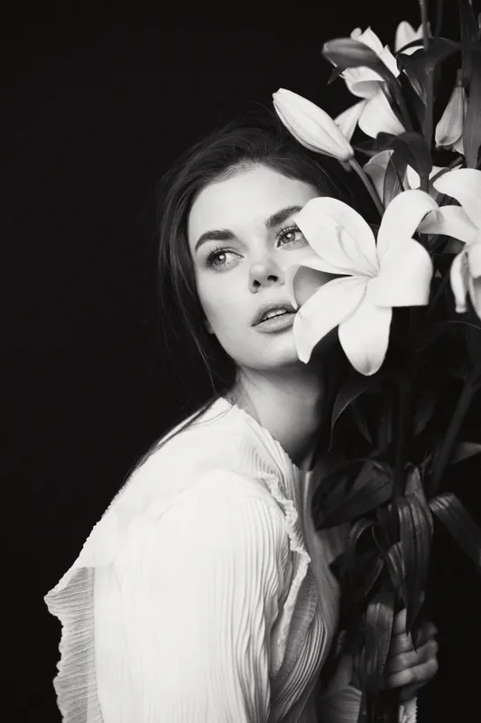 Beautiful model with white lilies, featuring an elegant outfit, expressing soft emotions in a black and white style, perfect for flower and beauty themes