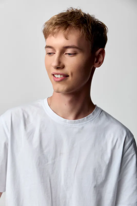 Young man with a soft smile wears a white tshirt in a studio setting, relaxed pose, clean light backdrop and calm, natural vibe for casual fashion and lifestyle projects