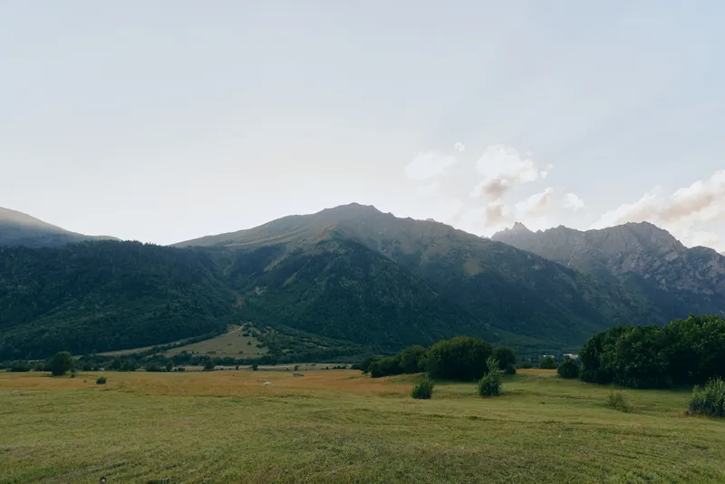 Open field with distant mountains under a clear sky, capturing vast landscape, nature, and calm. Wide horizon, gentle light, and quiet atmosphere convey solitude and freedom.