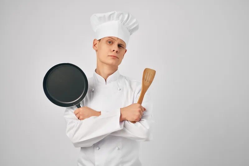 Шеф-повар держит в руках сковороду на кухне ресторана, занимаясь приготовлением пищи