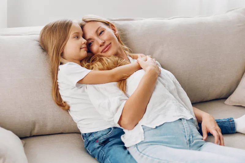 Мать и дочь разделяют радостный момент на уютном диване на фоне чистого белого фона