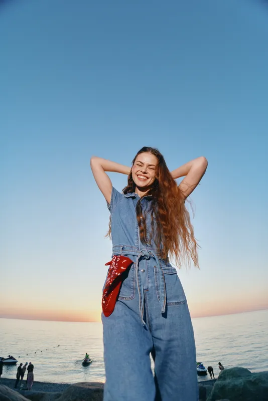 joyful woman in modern boho-western denim outfit smiling outdoors at sunset with film color, casual lifestyle, street style, relaxed atmosphere