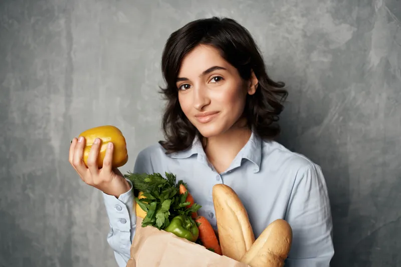 Женщина в синей рубашке держит пакет с продуктами здорового питания