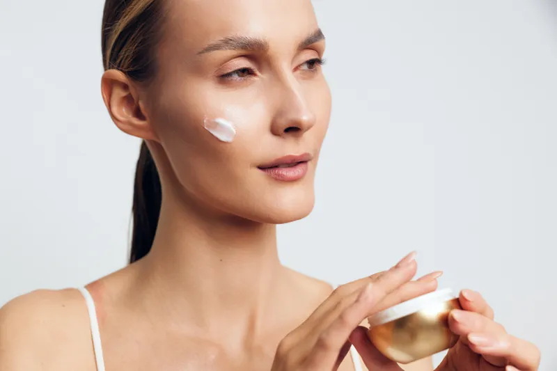 Young woman applies face cream with gentle expression skincare beauty routine closeup natural skin care health concept isolated on white background.