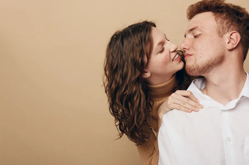 Young couple in casual clothes shares intimate moment, woman gently touching man’s shoulder and smiling with closed eyes. Concept of love, affection, and romantic connection.