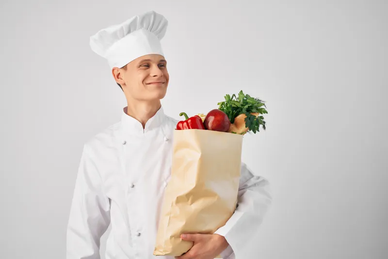Мужчина в форме шеф-повара с пакетом продуктов занимается работой и обслуживанием