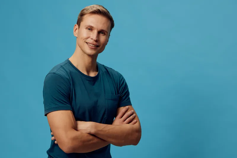 smiling man in teal t-shirt crossed arms look camera isolated on blue background digital nomad confidence lifestyle concept