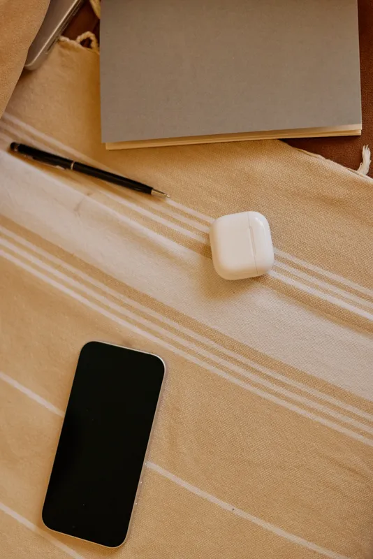 Cozy home workspace with a phone, notebook, pencil, and case beside earbuds on a striped blanket, creating a calm study mood and everyday personal routine in a warm setting