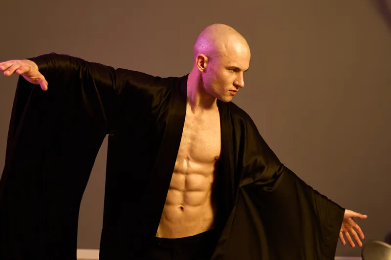 Dynamic and captivating man in a flowing black robe, showcasing strength and grace, with a strong pose that highlights his toned physique and artistic flair.