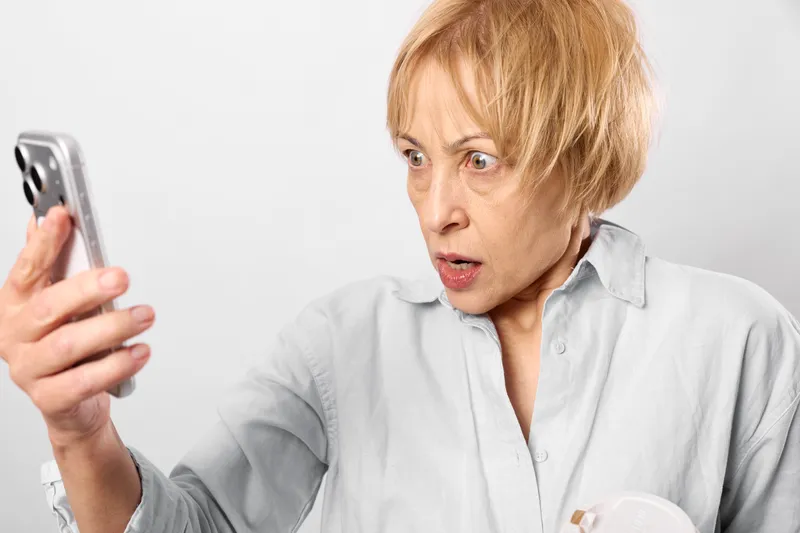 Surprised woman with short hair holding smartphone for communication, closeup on face, indoor white studio background, expression of surprise, lifestyle moment