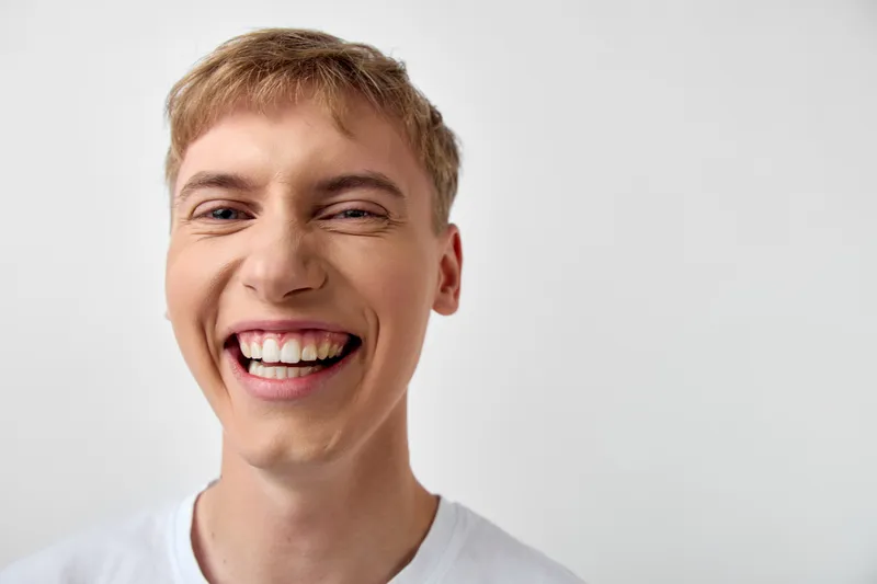Smiling man with bright expression and joyful smile, close up shot in a clean background, white t shirt, conveying happiness, energy and positive lifestyle mood