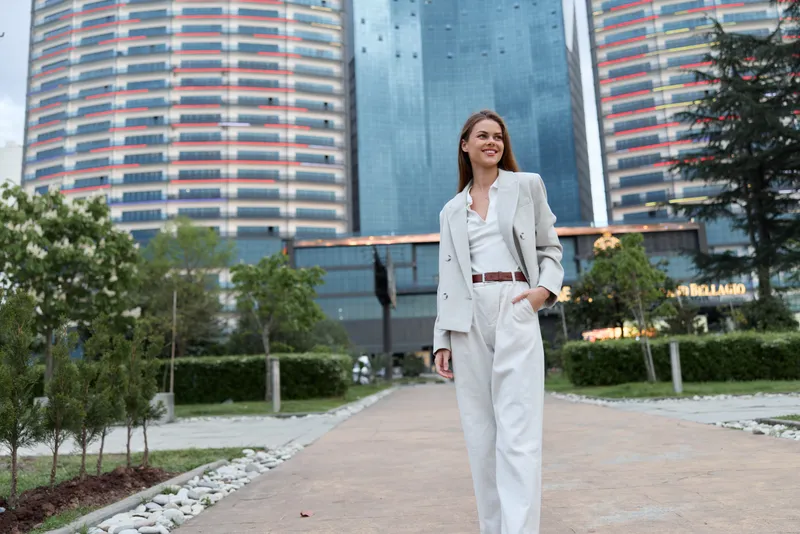 Confident businesswoman in stylish suit walking through modern urban setting with greenery and contemporary architecture. Perfect for business-related themes.