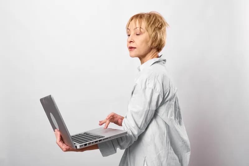Woman with laptop typing in a studio, side view, focused expression, white background, casual shirt, modern office atmosphere soft light, calm mood today