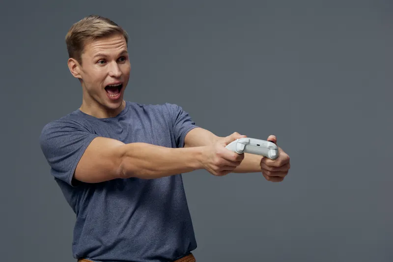Enthusiastic young man playing video game holding gamepad smiling excited face casual t-shirt studio shot gray background people entertainment concept