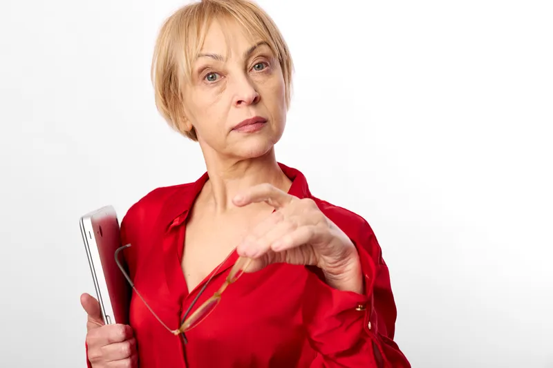 Elderly woman smartphone technology communication pointing portrait studio, red blouse, holding phone and pointing finger, thoughtful mood, white background