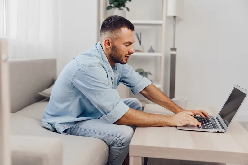 Focused man working on laptop in a stylish, modern living room, embodying creativity and productivity in a contemporary home office setting.