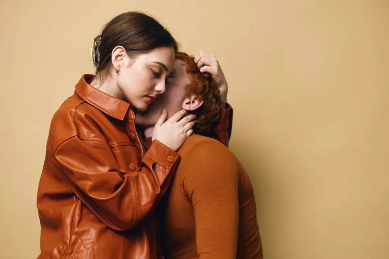 Woman comforting friend in warm brown clothing on beige background for support, empathy, emotional connection, care, friendship, and compassion between two people.