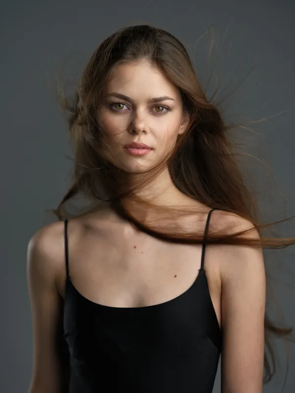 Portrait of a serious woman with freckles and windblown hair wearing a black top on a neutral background.