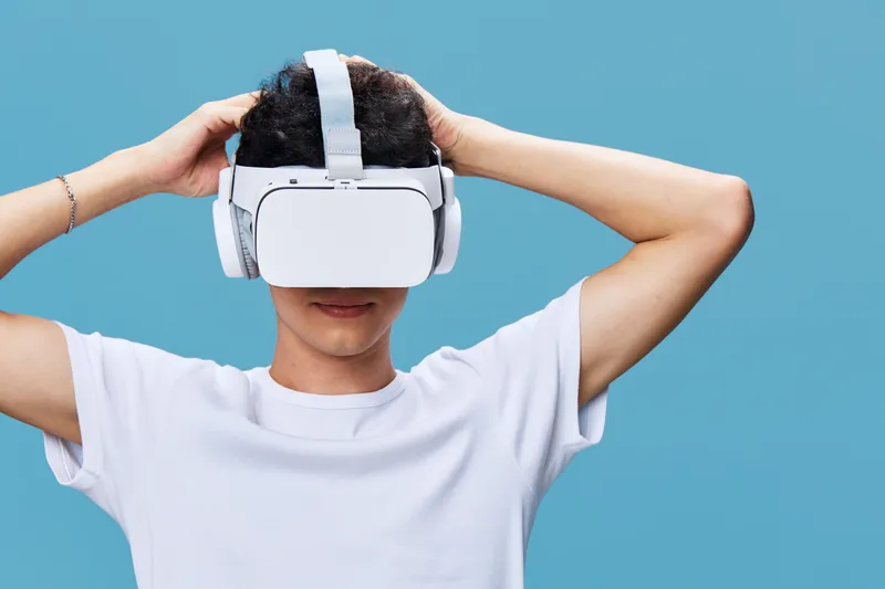 Young man with VR headset exploring virtual reality, wearing casual white t-shirt, on bright blue background, modern digital technology experience.