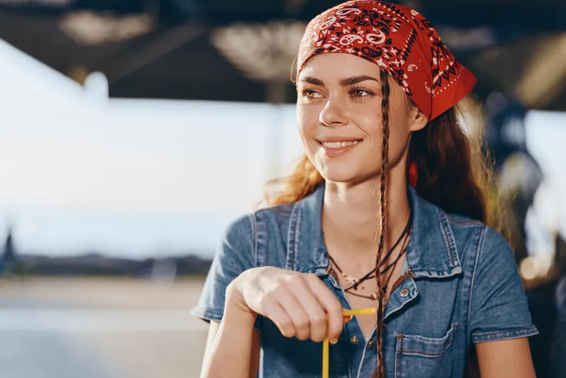 Lifestyle woman in modern boho-western denim street style with braided hair and red bandana, captured in warm film color tones, relaxed and stylish outdoors.