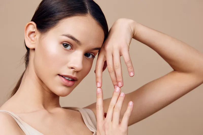 Elegant young model posing gently with hands against a soft beige background, showcasing natural beauty, serenity, and minimalism in fashion photography