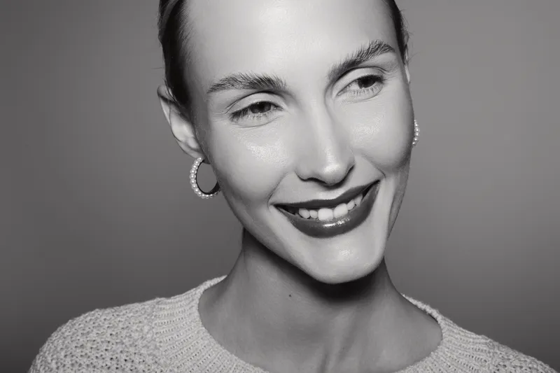 Smiling caucasian woman with fair skin and short hair wearing earrings and a knitted sweater in black and white studio lighting. Concept of happiness and natural beauty.