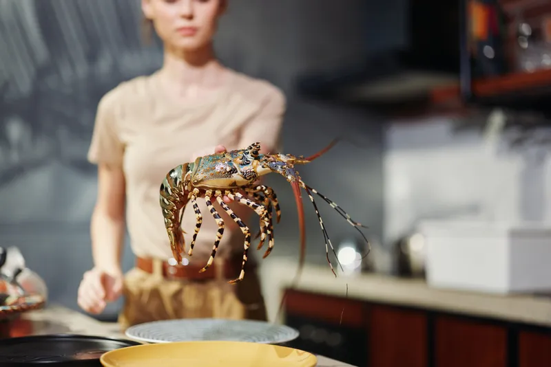 Женщина готовит свежего лобстера на сковороде на кухне, приготавливая вкусное блюдо из морепродуктов дома