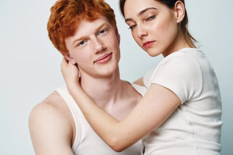 Young couple with red hair man and woman embracing, closeup portrait with white shirts on plain background, relationship, affection, love and intimacy with skin details.