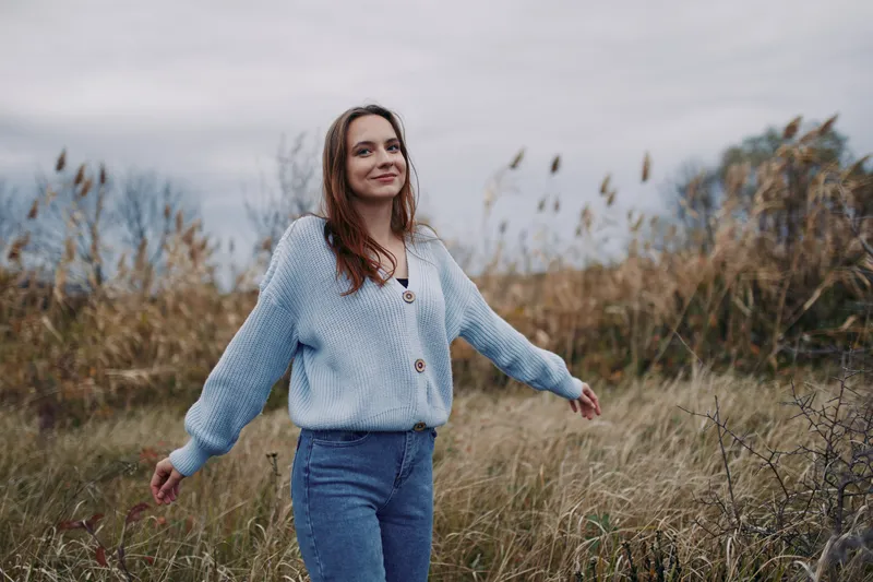 Candid portrait of a woman in a soft knit sweater strolling through a grassy field, conveying authenticity, calm presence, and natural, effortless style.