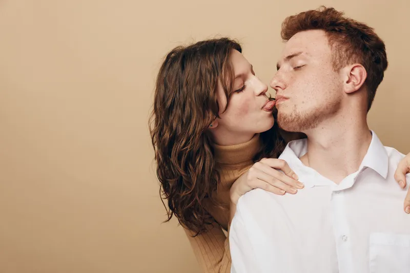 Young couple in casual clothes shares a tender moment with a gentle kiss on beige background. Concept of love, intimacy, affection, and romantic relationship between partners.