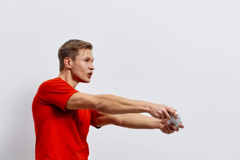 Over 50 man in red t-shirt playing video game holding game controller in hands, focused and excited, isolated on plain light gray background, studio shot, entertainment and gaming concept