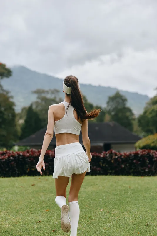 Young woman jogging in sporty white outfit in nature, showcasing fitness and health concepts with lush greenery in the background