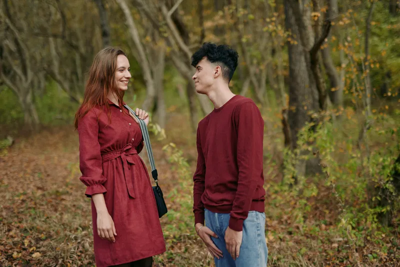 Authenticity and credibility shine as a candid moment unfolds between a couple in a quiet park, dressed in burgundy tones, natural expressions, and soft autumn light.