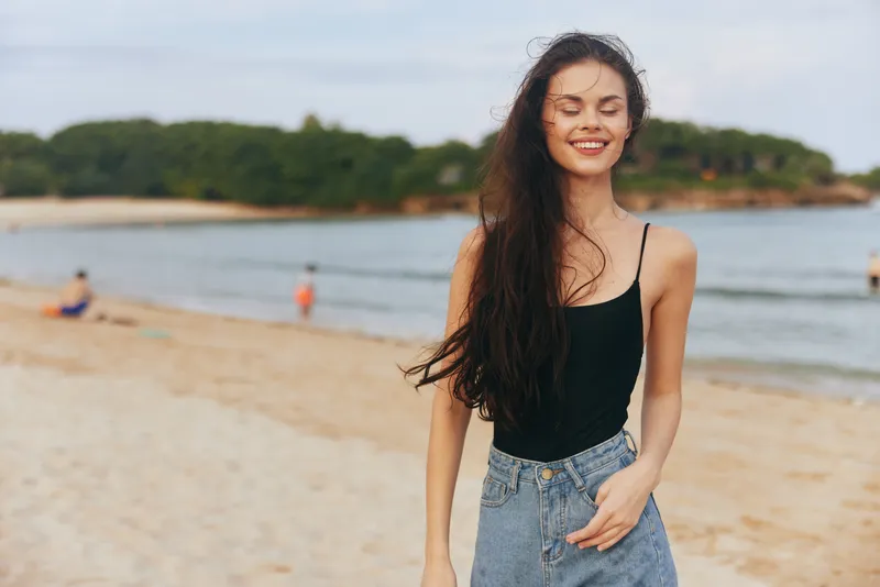 Женщина улыбается на пляже, наслаждаясь отдыхом и закатом