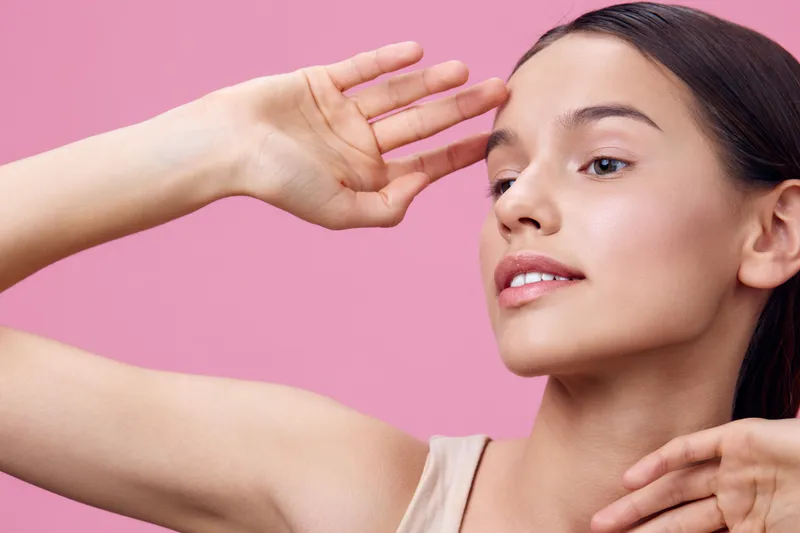 Portrait of a young woman with natural makeup and elegant hairstyle against a pink background, conveying beauty and grace, ideal for lifestyle and wellness concepts