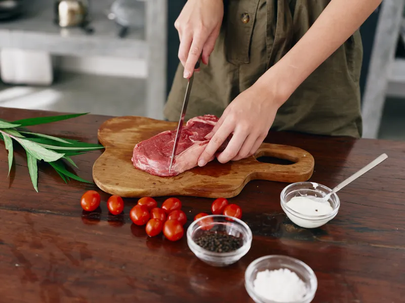 Женщина с ножом в руке нарезает стейк для жарки на кухне
