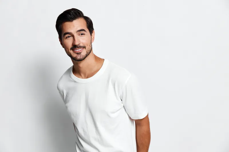 Smiling man dressed in a casual white t-shirt, looking at the camera with a friendly expression against a plain light background. People lifestyle concept.
