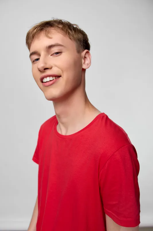 Young man wearing a red shirt, smiling warmly, casual studio setting with a bright neutral backdrop, relaxed pose conveying friendly energy, ideal for lifestyle, youth fashion, and positive everyday