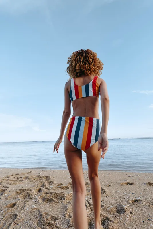 Beach ocean sky swimsuit woman walking back view summer vacation on sandy shore, adult female in colorful striped swimwear facing horizon, calm waves and sunlight, leisure carefree mood