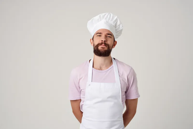 Мужчина-повар в фартуке жестикулирует рукой, выражая эмоции на кухне на светлом фоне